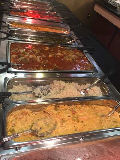 A buffet display featuring various trays of pasta, rice, and sauces in a restaurant setting.