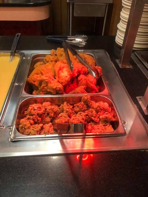 A buffet tray filled with crispy fried chicken pieces and a serving utensil on a dark countertop.
