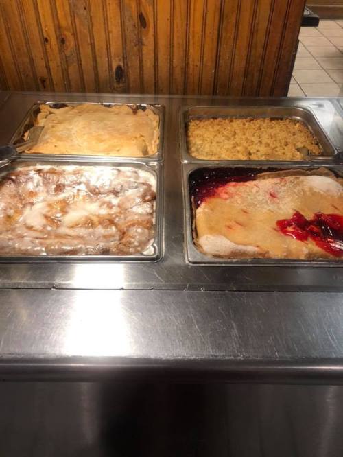 Four trays of desserts, including cobbler and pudding, displayed on a stainless steel counter.