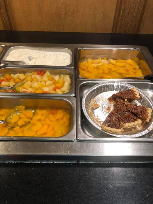 A buffet table with various fruit salads, a bowl of cottage cheese, and a pie slice on a plate.