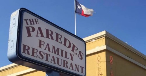 Sign for Paredes Family Restaurant with a Texas flag flying above against a clear blue sky.