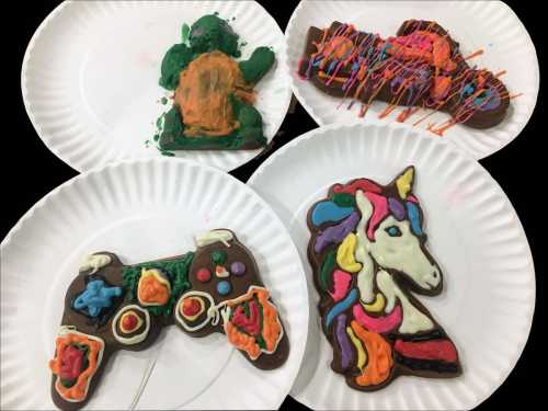 Four decorated chocolate shapes on paper plates: a turtle, a colorful abstract design, a game controller, and a unicorn.