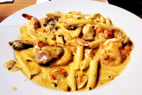 A plate of creamy pasta with shrimp, mussels, and penne, garnished with herbs and spices.