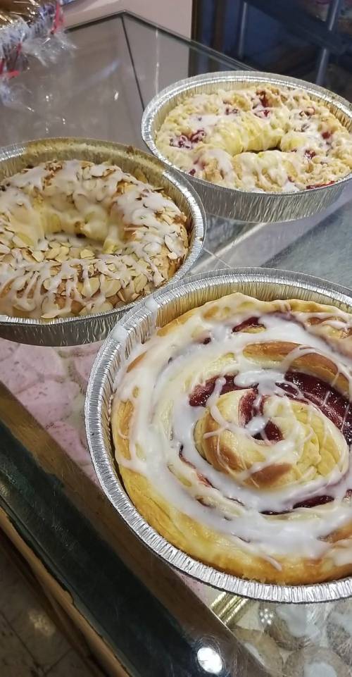 Three delicious pastries in aluminum trays: one topped with almonds, one with a cherry filling, and a cinnamon roll.
