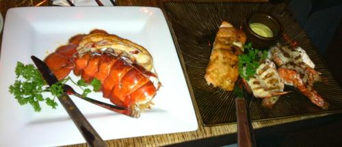 A plate with lobster tail and a side of grilled shrimp, garnished with parsley and served with a dipping sauce.