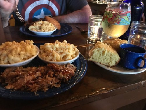 A table setting with two bowls of macaroni and cheese, pulled pork, cornbread, and a drink in a glass.
