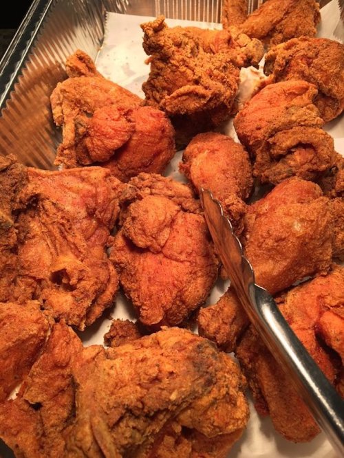 A tray of golden-brown fried chicken pieces, some whole and others cut, with tongs resting on the side.