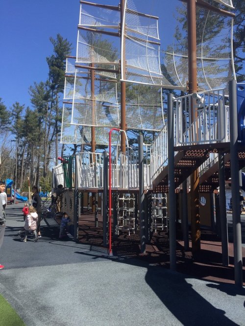 A playground featuring a large pirate ship structure with climbing nets and slides, surrounded by trees.