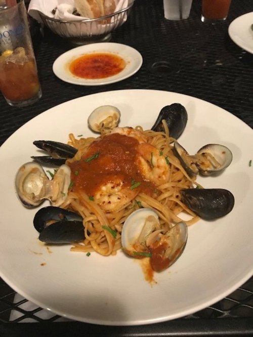 A plate of spaghetti topped with marinara sauce, shrimp, and clams, served with a side of sauce and a drink.