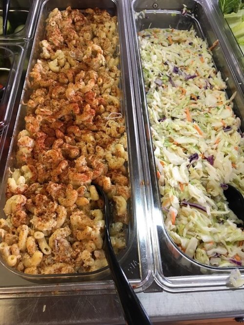A buffet tray with macaroni salad on the left and coleslaw on the right, both served with black serving spoons.