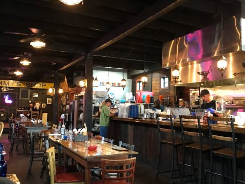 Interior of a cozy diner with wooden tables, a bar area, and staff preparing food in a warm, inviting atmosphere.