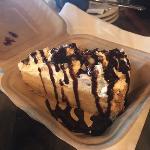 A slice of dessert in a takeout container, topped with whipped cream and chocolate drizzle.
