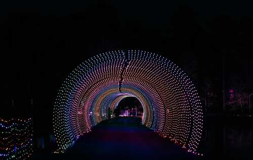 A brightly lit tunnel of colorful lights against a dark background, creating a festive atmosphere.