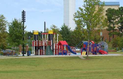 Colorful playground with slides, climbing structures, and towers, surrounded by green grass and trees.