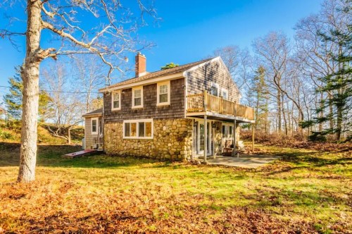 A charming two-story house with a stone exterior, surrounded by trees and autumn leaves under a clear blue sky.
