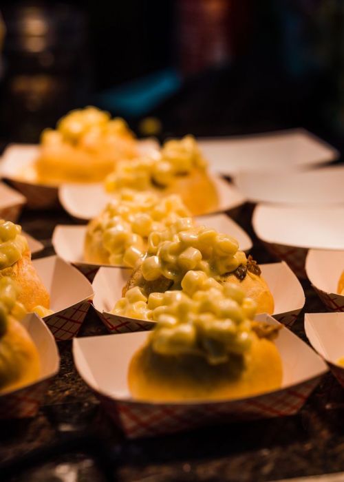 Close-up of small buns topped with creamy macaroni and cheese, arranged on a dark surface.