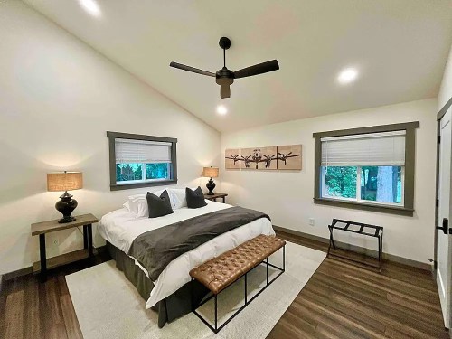 Cozy bedroom with a king bed, two lamps, a bench, and large windows overlooking greenery. Modern decor and warm tones.