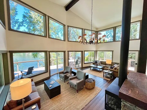 Bright, modern living room with large windows overlooking a lake, featuring comfortable seating and stylish decor.