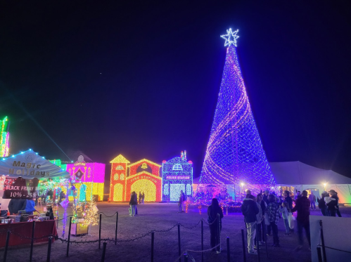 A festive scene at night featuring a large illuminated Christmas tree and colorful holiday lights, with people enjoying the display.