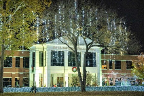 A building decorated with festive lights and wreaths, surrounded by trees illuminated for the holiday season at night.