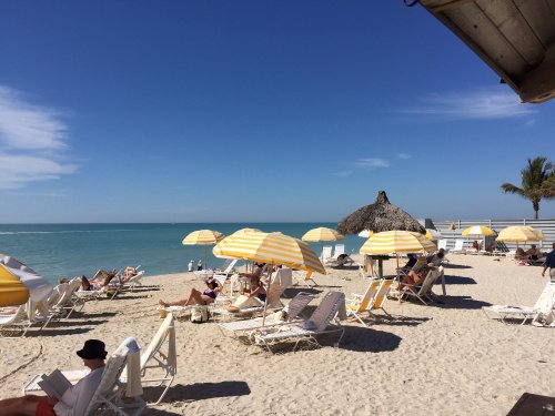 A sunny beach scene with yellow-striped umbrellas, lounge chairs, and a thatched hut by the calm blue ocean.