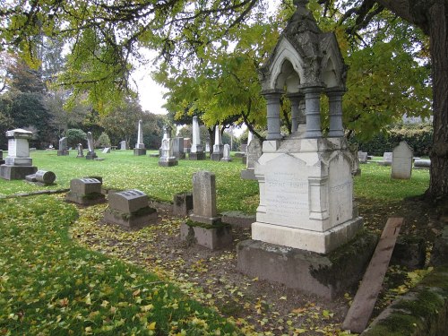 A serene cemetery scene with gravestones and a decorative monument surrounded by fallen leaves and trees.