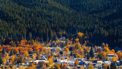 Aerial view of a small town surrounded by vibrant autumn foliage and dense evergreen forests.