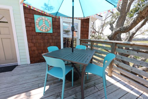 A patio with a table and four turquoise chairs under a blue umbrella, surrounded by trees and a peaceful view.