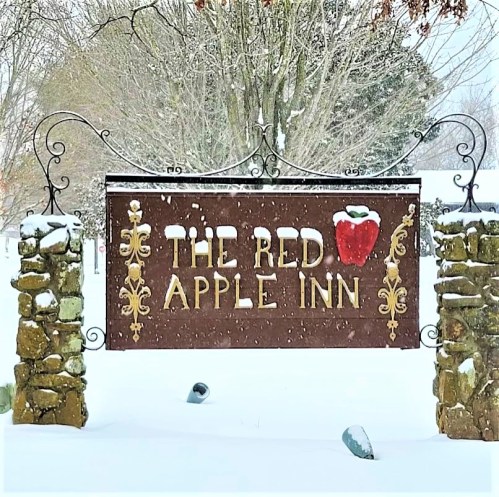 Sign for "The Red Apple Inn" surrounded by snow-covered trees and a snowy landscape.