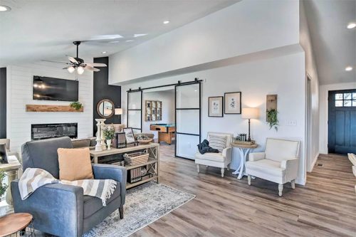 A modern living room with a cozy seating area, fireplace, and sliding barn door, featuring light wood floors and decor.
