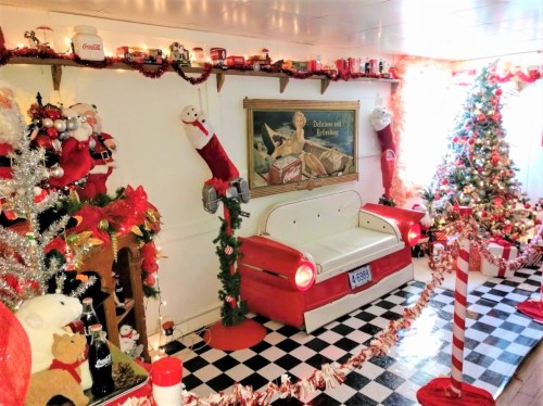 A festive room decorated with Christmas trees, stockings, and a vintage red couch, creating a cheerful holiday atmosphere.