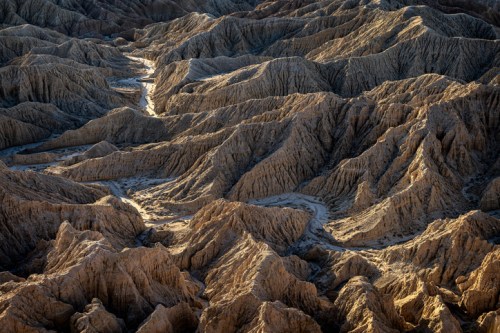 A rugged landscape of textured, undulating hills and valleys, illuminated by warm sunlight.