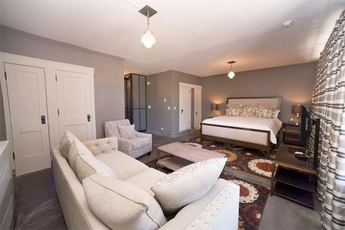 A spacious hotel room featuring a king bed, seating area, and modern decor with neutral tones and patterned curtains.