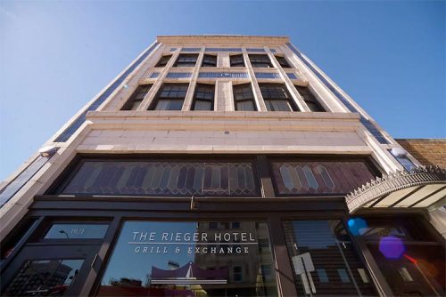 View of the Rieger Hotel Grill & Exchange, showcasing its tall facade and entrance under a clear blue sky.