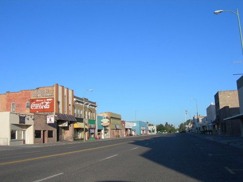 A quiet street in a small town, featuring vintage storefronts and a clear blue sky.