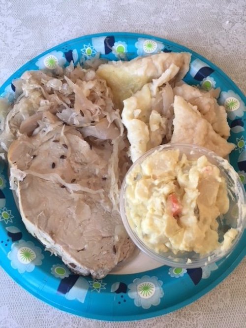 A blue paper plate with sliced turkey, sauerkraut, dumplings, and a cup of potato salad.