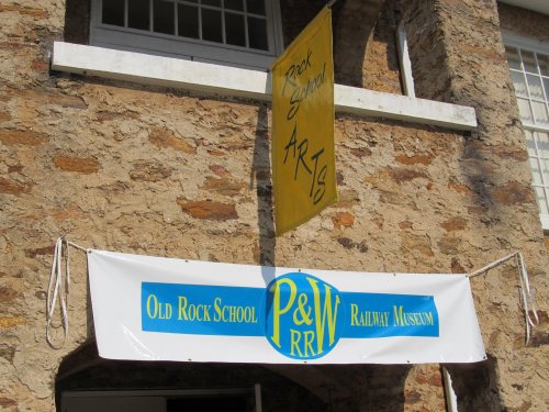 Signage for Old Rock School and P&W Railway Museum, featuring a yellow banner for arts events.