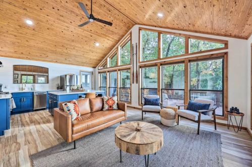 Cozy living room with wooden ceiling, large windows, a leather sofa, and a round coffee table, surrounded by nature.
