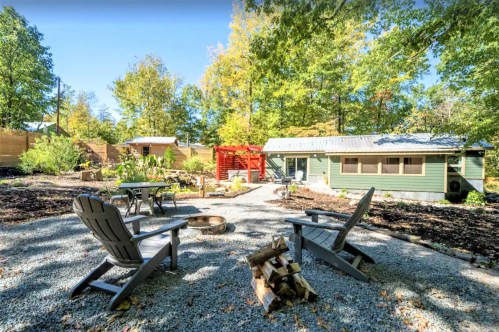 A cozy outdoor space with chairs around a fire pit, surrounded by trees and a small garden area.