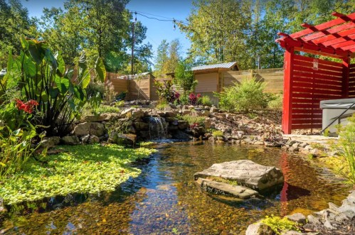 A serene garden with a pond, waterfall, lush greenery, and a red pergola in a peaceful outdoor setting.