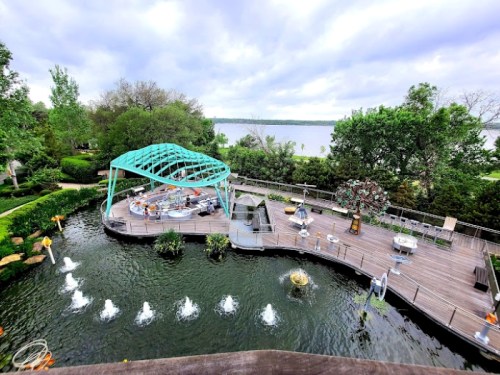 A scenic view of a landscaped area with a pond, fountains, and a turquoise gazebo overlooking a lake.