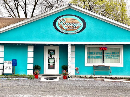 Bright turquoise restaurant exterior with a sign reading "Rossy's Place," featuring an open sign and flower pots.