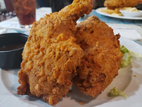 Two crispy fried chicken pieces on a plate, accompanied by a small bowl of dipping sauce and a garnish of lettuce.