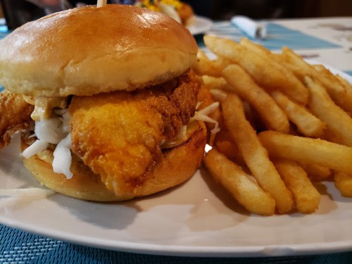 A crispy fried fish sandwich with coleslaw on a soft bun, served with a side of golden French fries.
