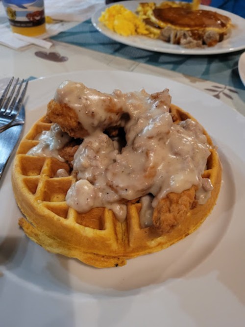 A golden waffle topped with crispy fried chicken and creamy gravy, served on a white plate with a fork.