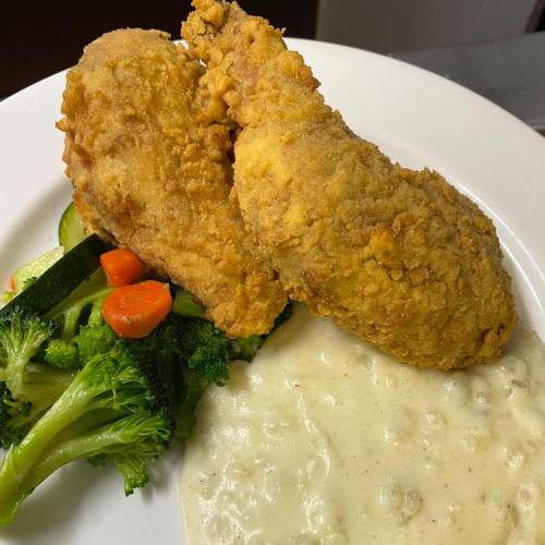 A plate featuring two crispy fried chicken breasts, creamy gravy, and a side of steamed broccoli and mixed vegetables.