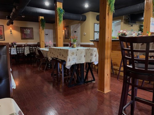 Interior of a cozy restaurant with wooden beams, tables covered in tablecloths, and a warm, inviting atmosphere.