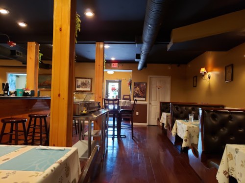 Interior of a cozy restaurant featuring wooden beams, tables with white tablecloths, and a warm, inviting atmosphere.