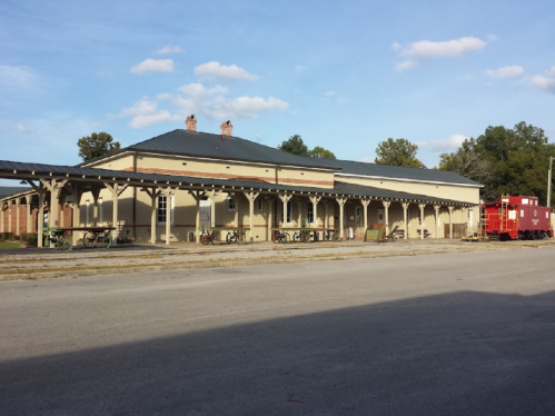 Historic train station with a red caboose, surrounded by trees and a clear blue sky.