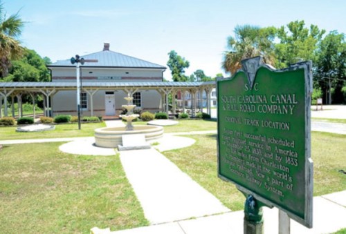 Historic South Carolina Canal and Railroad Company site with a green sign and a fountain in a grassy area.